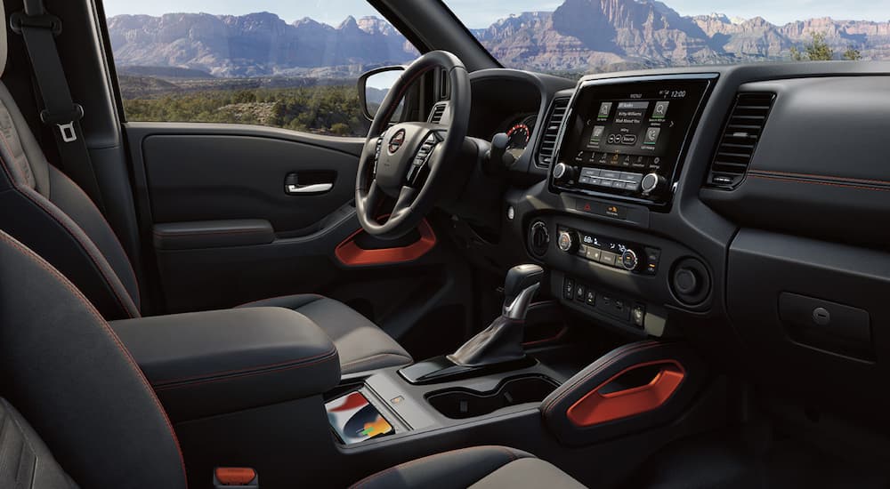 The black interior of a 2023 Nissan Frontier Pro4x shows the steering wheel and infotainment screen.