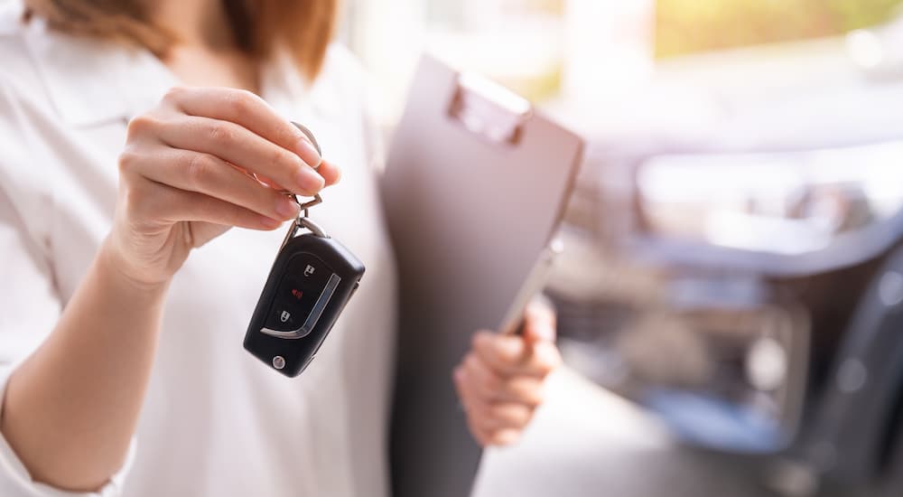 A saleswoman is shown holding a car key at a car dealership.