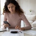 A person is shown budgeting with a phone and laptop.