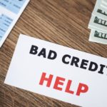 A notecard that says 'bad credit help' is shown on a table next to a calculator and money.