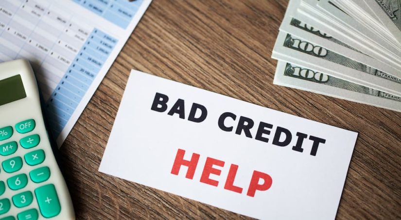 A notecard that says 'bad credit help' is shown on a table next to a calculator and money.