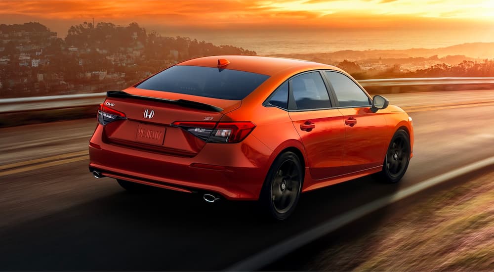 An orange 2022 Honda Civic Si is shown driving at sunset.