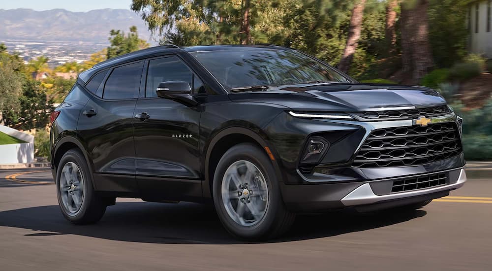 A black 2023 Chevy Blazer is shown driving up a tree-lined road.