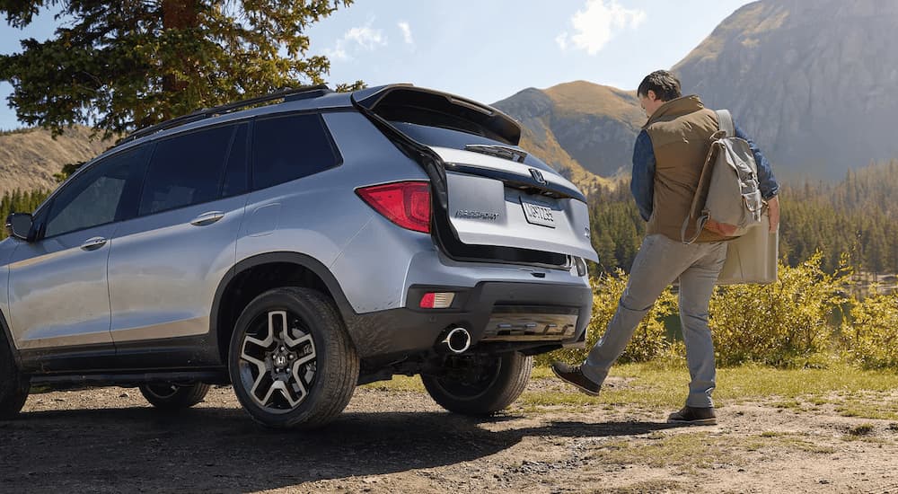 A man is shown opening the rear liftgate on a grey 2023 Honda Passport Elite.
