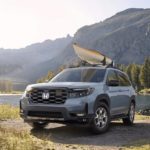 A grey 2023 Honda Passport Trailsport is shown parked with a kayak on the roof next to a lake.