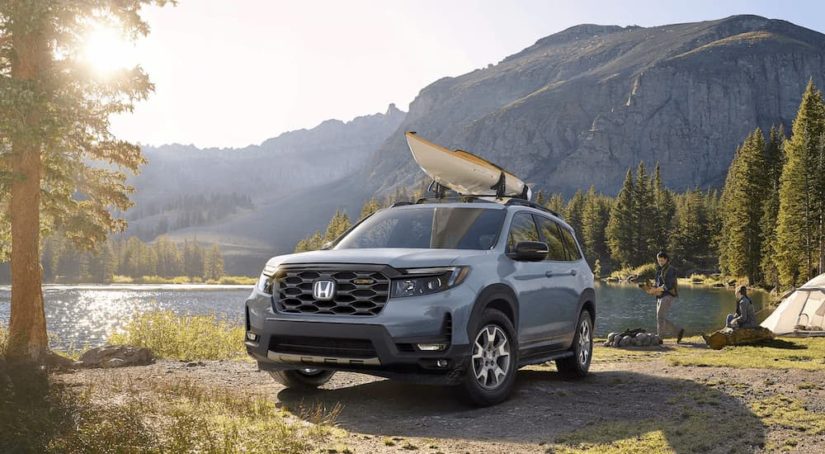 A grey 2023 Honda Passport Trailsport is shown parked with a kayak on the roof next to a lake.