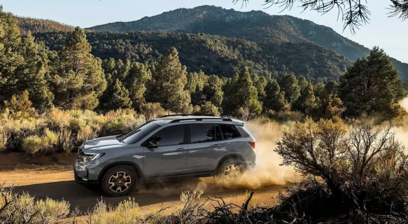 A grey 2023 Honda Passport Trailsport is shown driving on a dusty trail.