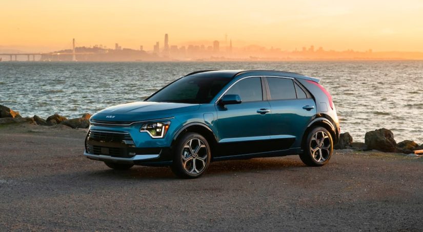 A blue 2023 Kia Niro PHEV is shown in front of a city across a bay.