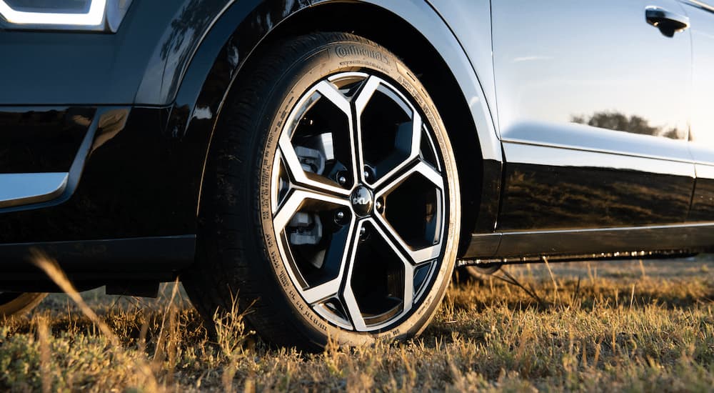A close up of the tire on a black 2023 Kia Niro is shown while parked in a field.
