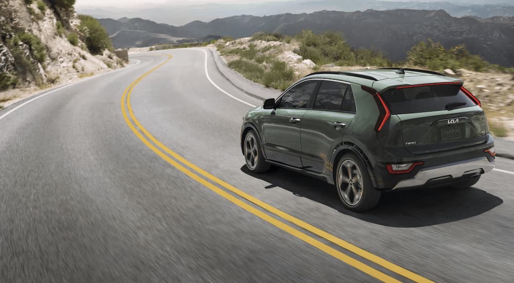A green 2023 Kia Niro is shown driving on a winding road in the mountains.