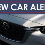 A close up shows the grille on a white 2024 Mazda CX-90 under a new car alert banner.