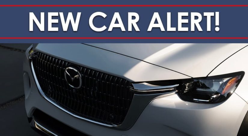 A close up shows the grille on a white 2024 Mazda CX-90 under a new car alert banner.