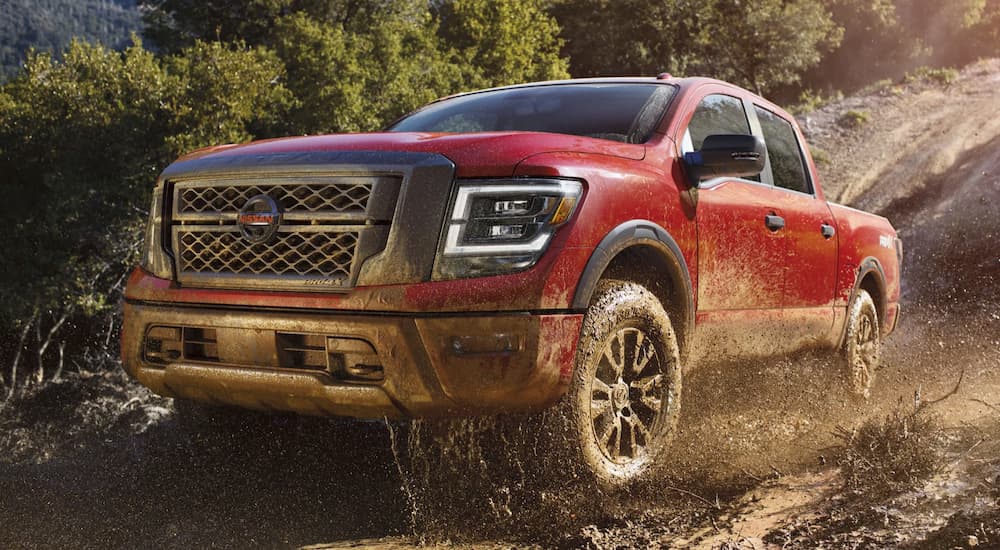 A red 2023 Nissan Titan XD Pro-4x is shown driving on a muddy trail.