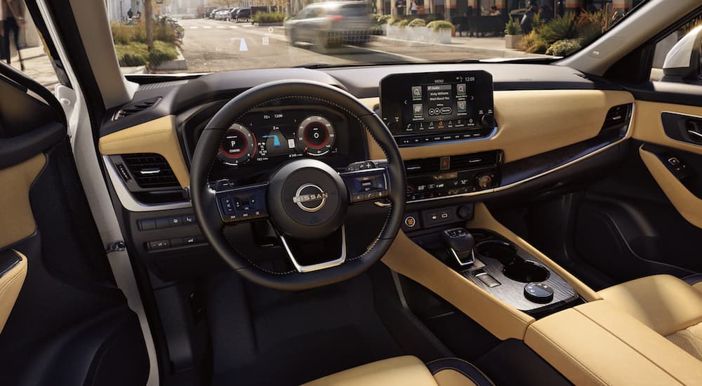 The black and yellow interior of a 2023 Nissan Rogue shows the steering wheel and infotainment screen.