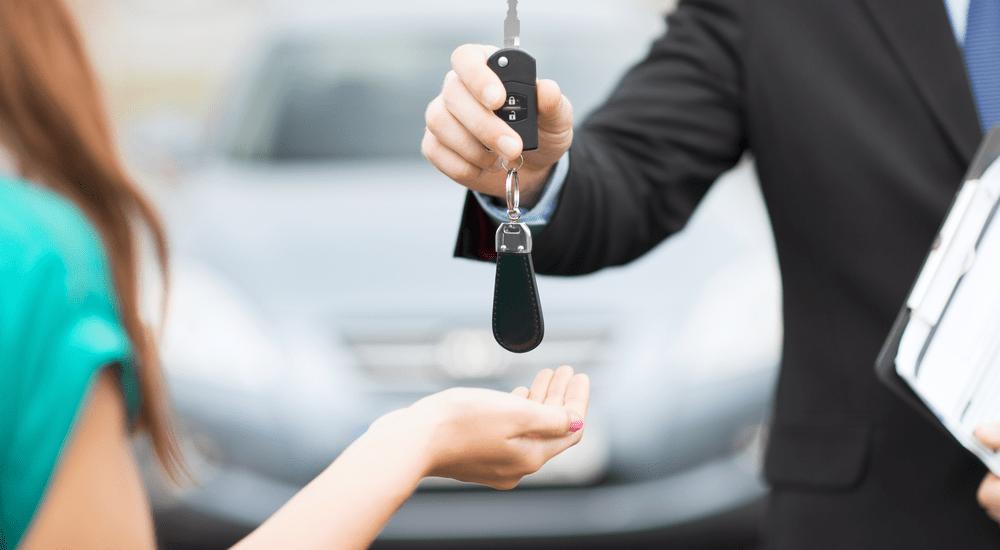 A salesperson is shown handing a car key to a customer.