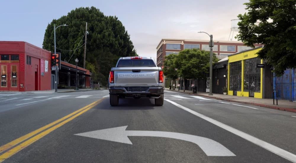 A silver 2023 Chevy Colorado Z71 is shown from the rear driving on a city street.