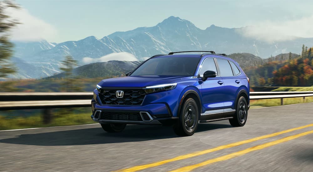 A blue 2023 Honda CR-V Sport Touring is shown driving on a mountain highway.