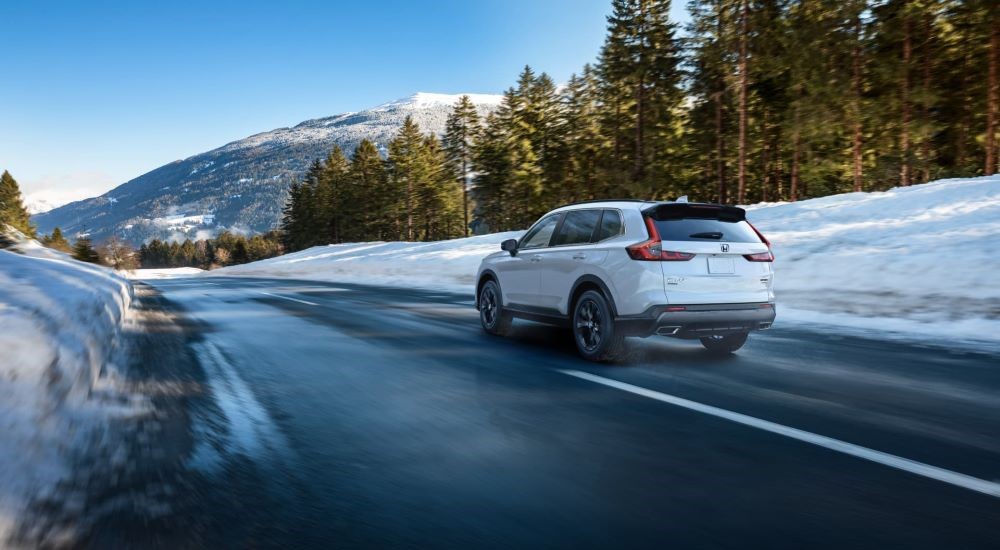 A white 2023 Honda CR-V is shown from the rear on a snowy road.