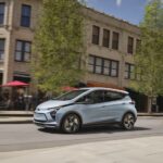 A blue 2023 Chevy Bolt EV is shown from the side on a city street.
