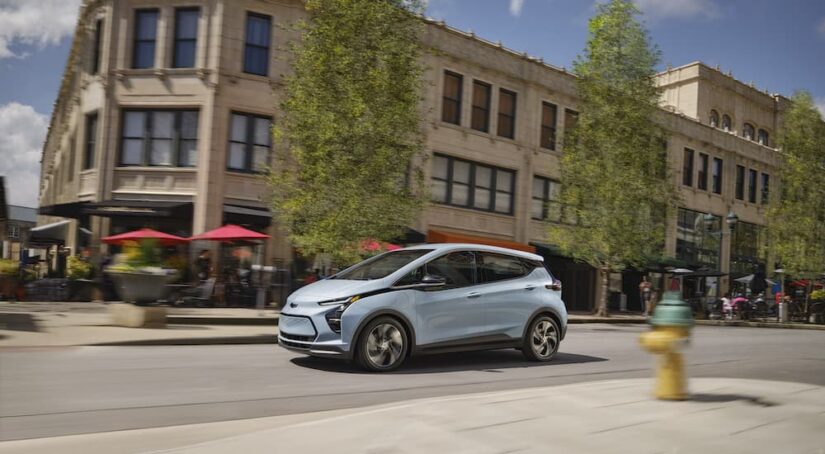 A blue 2023 Chevy Bolt EV is shown from the side on a city street.