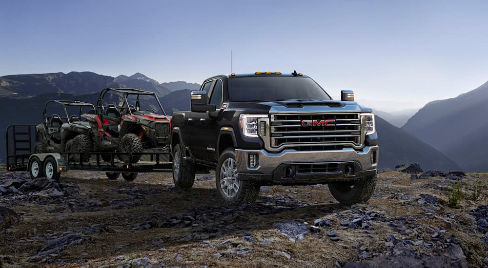 A black 2023 GMC Sierra 2500HD is shown from the front while towing UTVs.