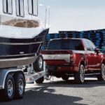 A red 2023 Nissan Titan XD is shown from the rear at an angle while towing a boat.