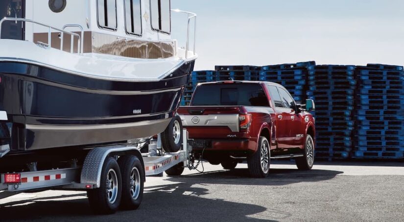 A red 2023 Nissan Titan XD is shown from the rear at an angle while towing a boat.