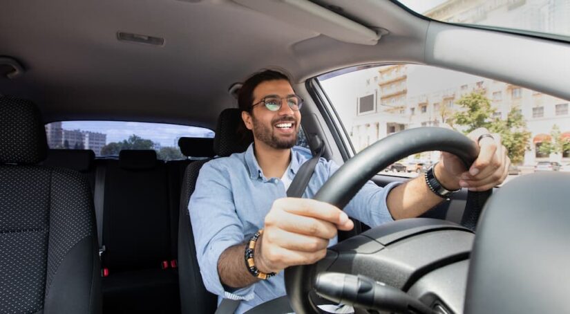 A man is shown driving a vehicle while smiling.