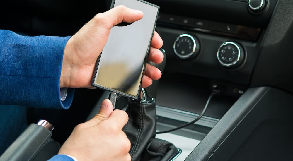 A person is shown plugging their phone into a charging cord in their vehicle.
