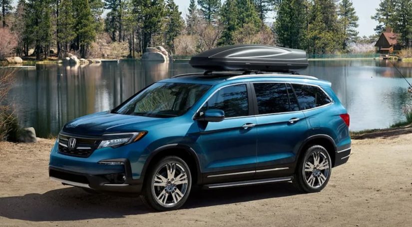A blue 2020 Honda Pilot is shown from the side parked next to a lake.