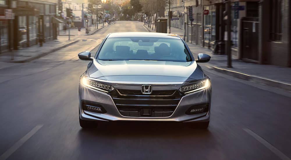 A silver 2021 Honda Accord is shown from the front driving on a city street after leaving a certified pre-owned Honda dealer.