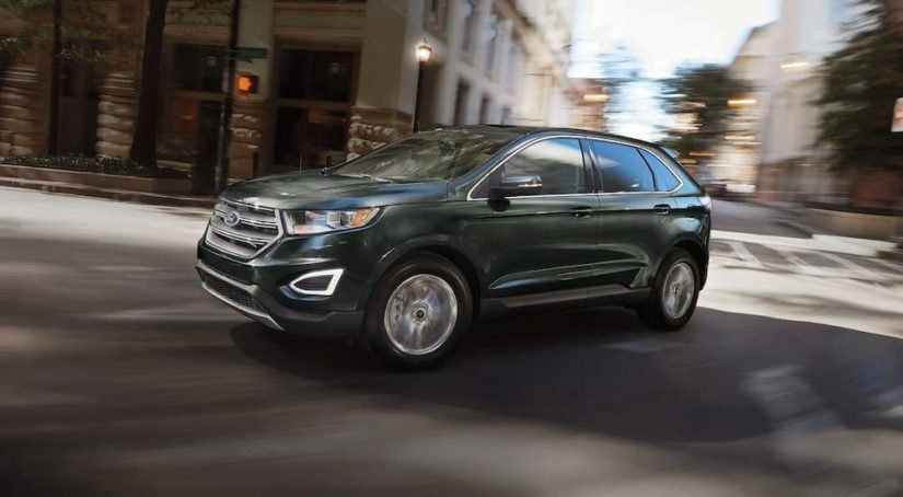 A green 2016 Ford Edge is shown driving on a city street after leaving a certified used SUV dealer.