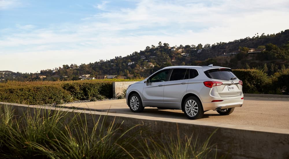 A silver 2019 Buick Envision is shown from the rear parked in a driveway surrounded by shrubs.