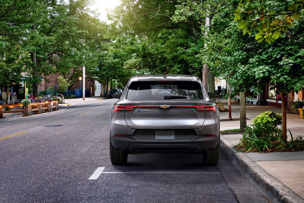 A grey 2024 Chevy Equinox EV 1LT is shown from the rear on a tree-lined street.