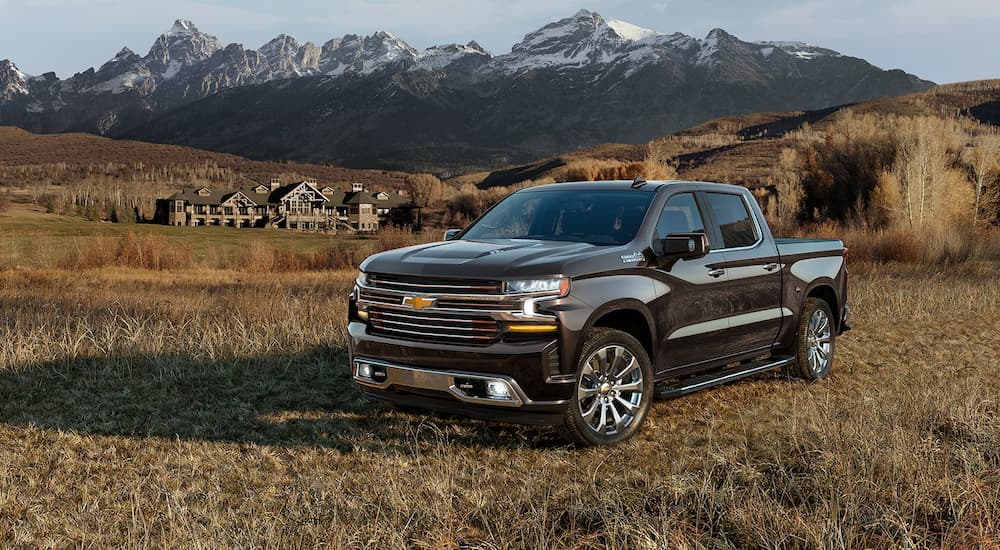 A black 2022 Chevy Silverado 1500 High Country is shown parked in a dry grassy field with a mountain view.