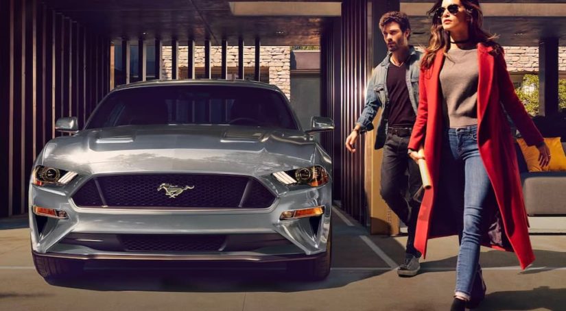 A couple is shown walking next to a silver 2021 Ford Mustang after leaving a used Ford dealer.