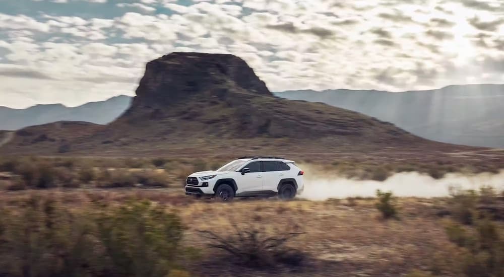 A white 2023 Toyota RAV4 is shown from the side while off-road.