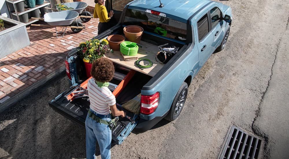 A woman is shown putting gardening supplies into the bed of a blue 2022 Ford Maverick.