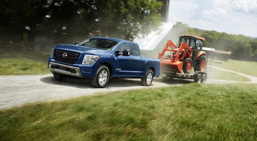 A blue 2023 Nissan Titan King Cab is shown towing a tractor on a dirt road.