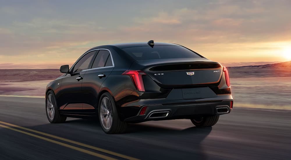 A black 2023 Cadillac CT4 drives down a highway into the setting sun.