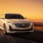 A white 2023 Cadillac CT5 is shown driving down a highway away from a Cadillac dealer.