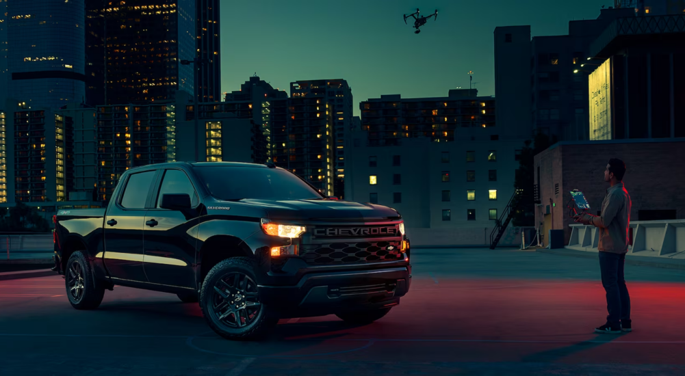 A man is shown flying a drone over a 2023 Chevy Silverado 1500 Custom with the Midnight Essentials package.