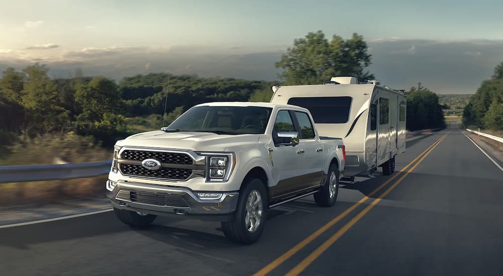 A white 2023 Ford F-150 is shown towing a white camper along a highway.