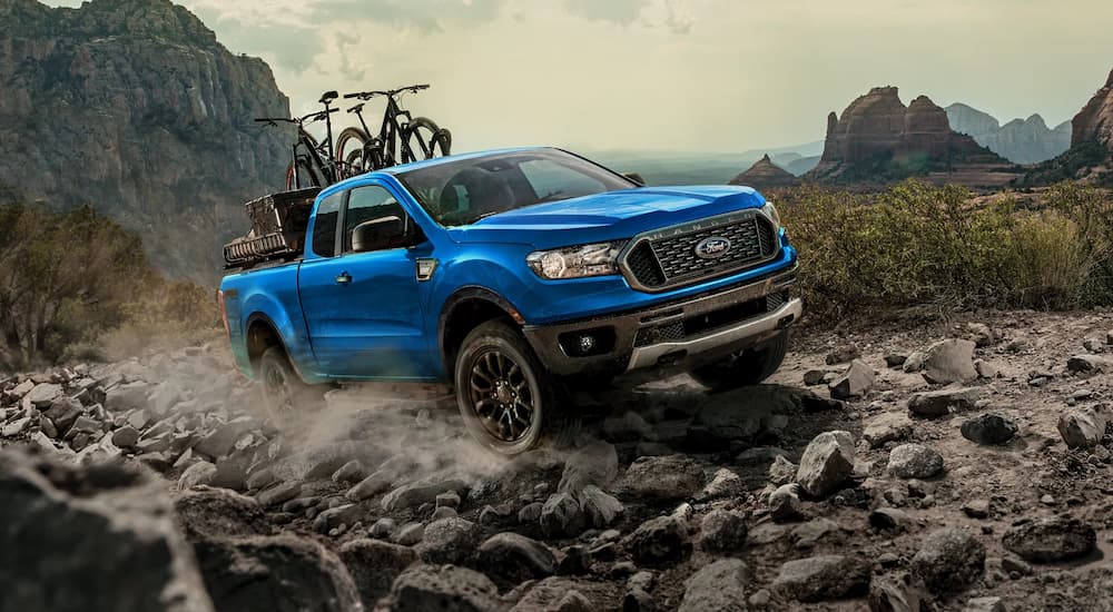 A blue 2023 Ford Ranger loaded with mountain bikes is shown climbing a rocky hill.