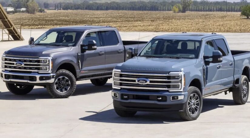 Two 2023 Ford Super Duty trucks in different shades of gray are parked side by side.