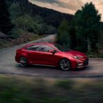 A red 2023 Toyota Corolla is shown from the side while taking a corner after leaving a Toyota dealer.