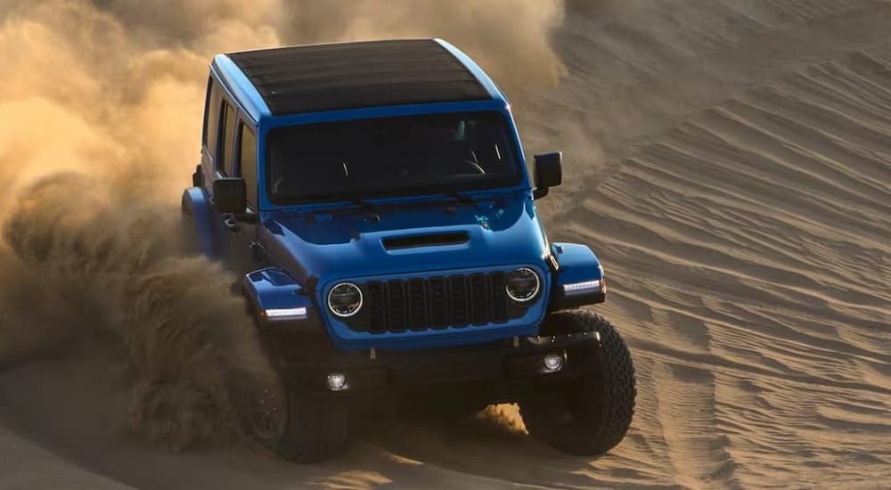 A blue 2024 Jeep Wrangler is shown driving off-road.