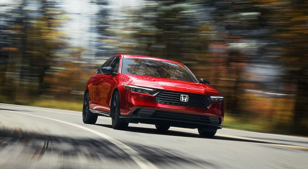A red 2023 Honda Accord Sport L is shown driving on a winding road.