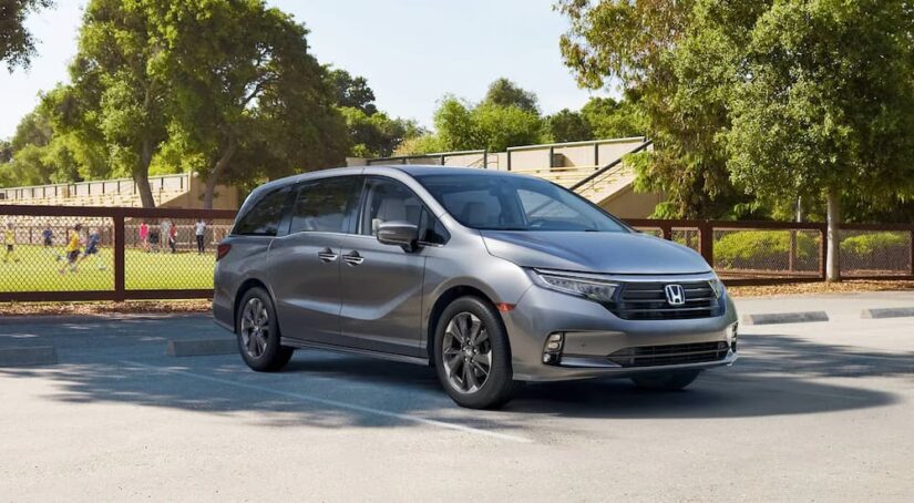 A silver 2023 Honda Odyssey is shown parked next to a soccer field.
