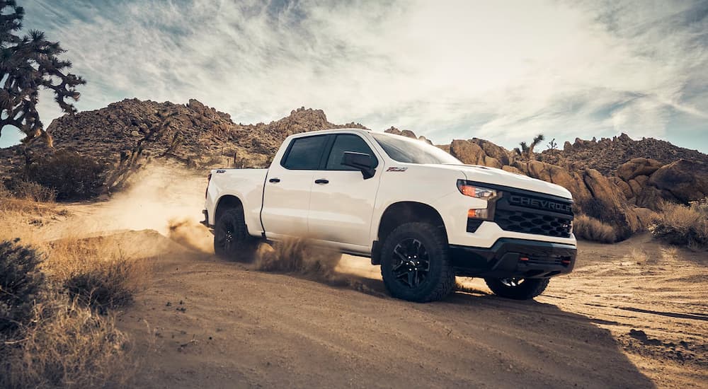 A white 2023 Chevy Silverado 1500 Z71 Custom Trail Boss is shown kicking up dust in the desert.